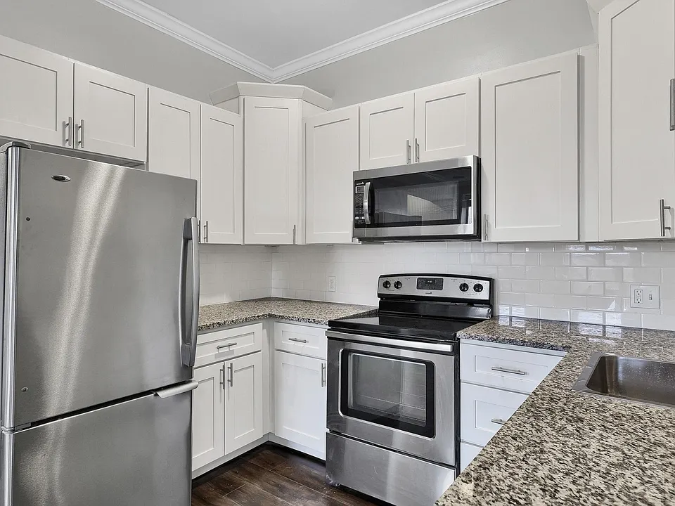 First-floor kitchen with granite countertops, white cabinetry, subway tile backsplash, dishwasher, and stainless steel appliances.