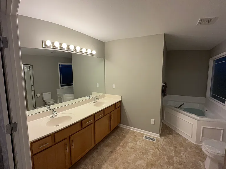 Master bedroom bathroom with dual sinks, new shower enclosure, toilet, and Jacuzzi tub with large light window.