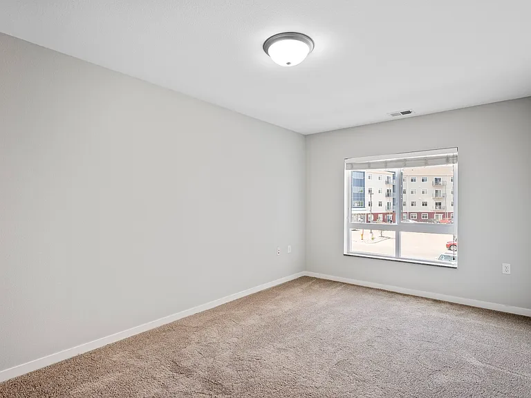 Bright bedroom with plush carpet and a large window offering urban views. Bright bedroom with plush carpet and a large window offering urban views.