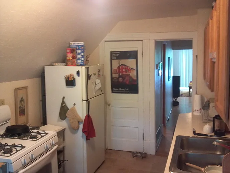 kitchen view of gas stove, refrigerator, closet that houses the furnace. View through to patio doors at the front of the apartment.