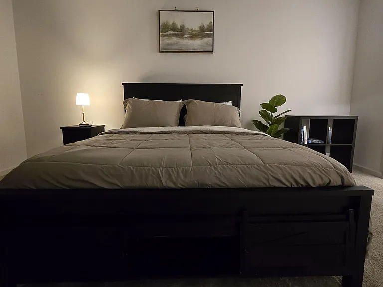 Furnished bedroom featuring a full-size bed, nightstand with lamp, and open shelving for books or storage.