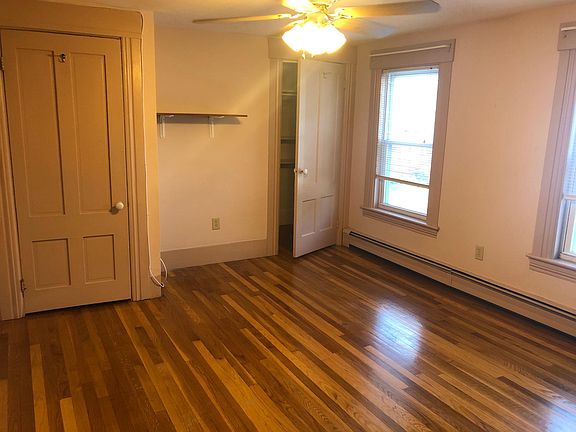 View of left side of master bedroom as seen from doorway. The two doors are for the closets. Two big windows and a ceiling fan and light, and a small shelf.