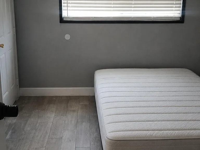 Simple bedroom with wood-look flooring, gray walls, and a wide window with blinds for privacy and light control.