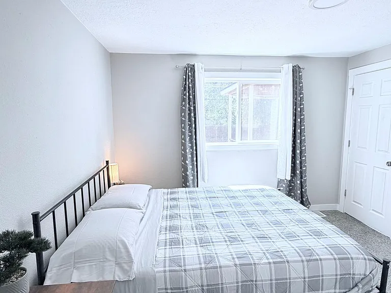 Private bedroom with a full-size bed, side table, and a window with curtains for natural light and privacy.