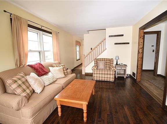 Sun filled living room with gleaming hardwood flooring leads to kitchen.