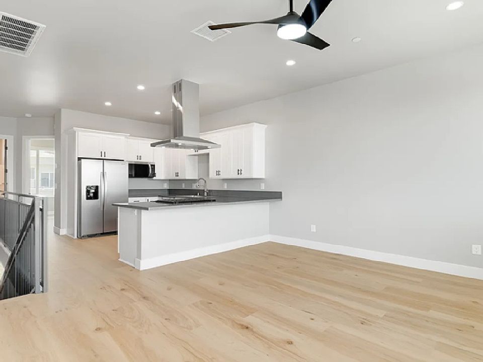 Open-concept great room with wide-plank light hardwood floors, recessed lighting, a modern ceiling fan, and an adjoining white kitchen.