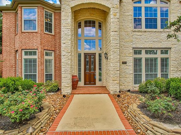 The white stone front porch is accented by the stately wooden door and glass side panels accessorized with a tall pottery planter and an antique sconce to welcome visitors.