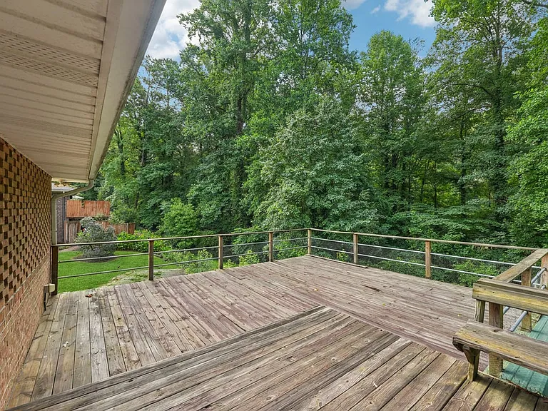 A charming woodland patio setting where the umbrella covered dining area, spacious deck, and leafy views create an inviting stage for fresh air and everyday wonder.