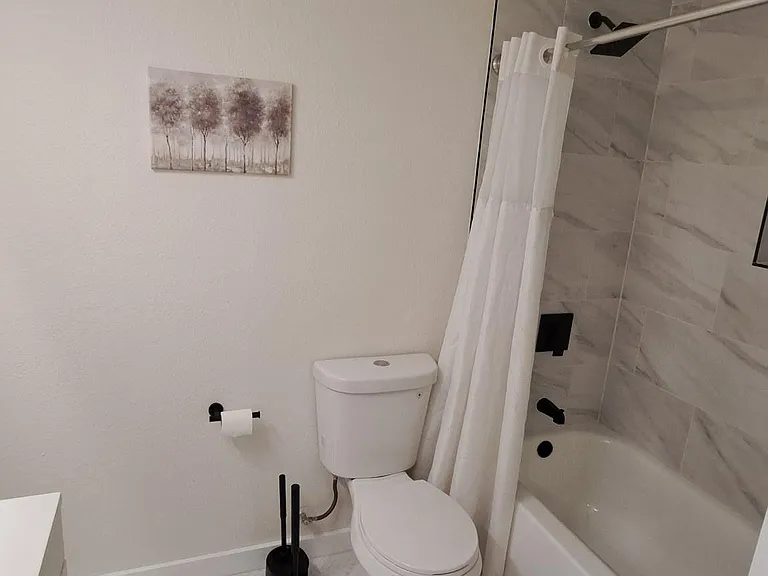 Clean full bath with tub/shower combo, tile surround, and matte-black fixtures, plus herringbone tile flooring.