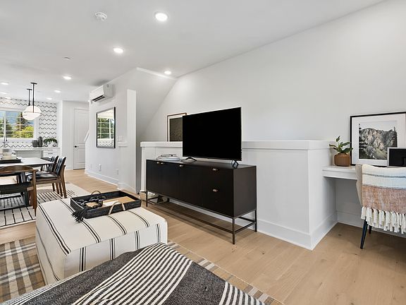 A modern and cozy living room with a television, a sofa, and a dining area visible, set against a ba