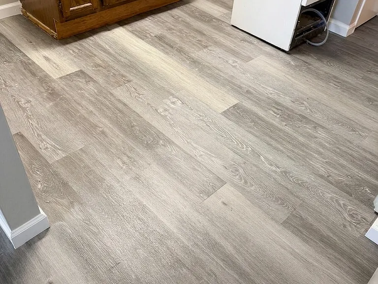 Detailed view of the kitchen space showcasing the wooden cabinetry, bright white baseboards, and the stunning new LVP flooring installed throughout.
