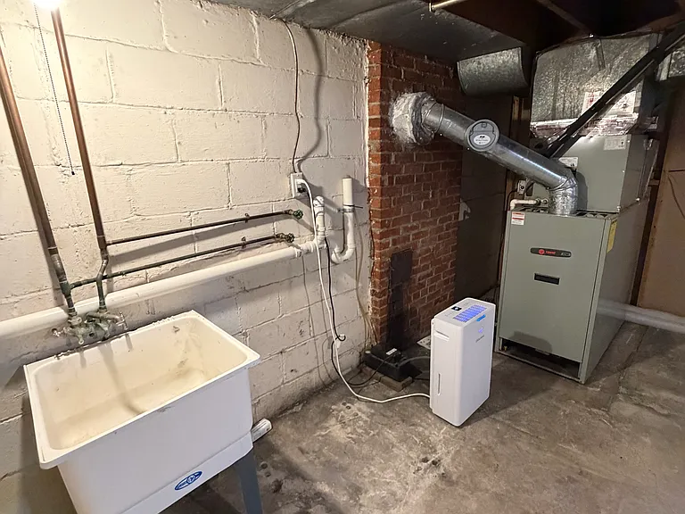 View of basement utility sink, new dehumidifier, high-quality Trane brand heat/AC unit with oil heat back-up system (installed 2016). All plumbing in house has been replaced with PVC.