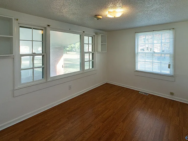 View of the front or 2nd bedroom showing the built-in shelves on either side of the front window & the side window. The closet is on the wall to the right, across from the front window, and the door to the room is behind the photographer.
