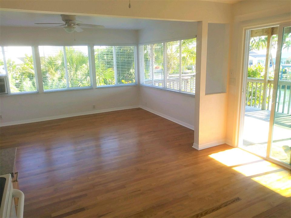 Living room with tons of natural light. Horizontal blinds on windows and vertical blinds on sliders for privacy. Ceiling fans and new heating-cooling unit. Wood flooring throughout the apartment has been completely refinished.