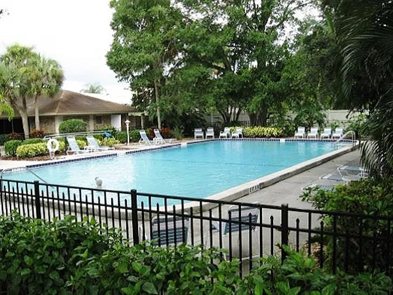 Large community pool, surrrounding fence, lounge chairs and tables, community clubhouse.