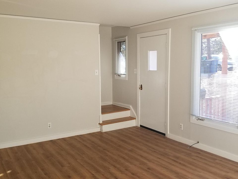 View from bright living room showing front entrance door, large living area windows, and landing/stairwell to upstairs.