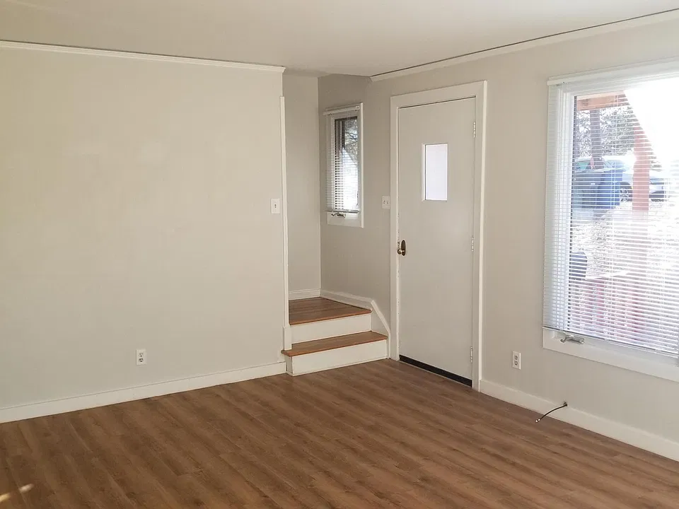 View from bright living room showing front entrance door, large living area windows, and landing/stairwell to upstairs.