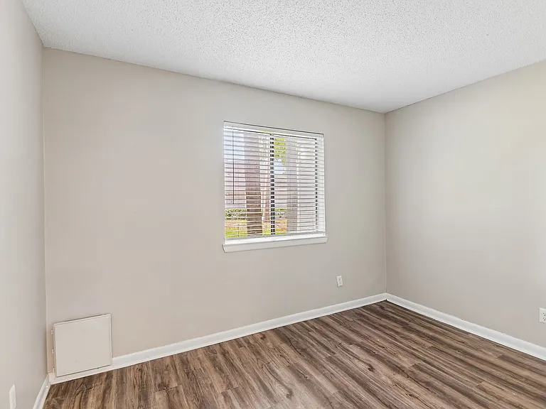 Bright and airy room with elegant neutral walls, rich hardwood flooring, and a window offering serene outdoor views.