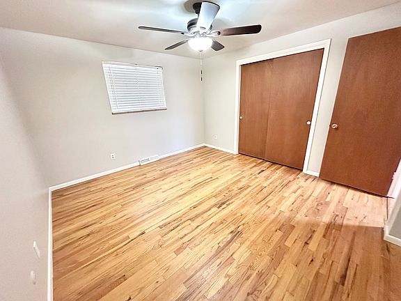 Bright and airy bedroom with elegant hardwood flooring, spacious wooden closets, and a modern ceiling fan.
