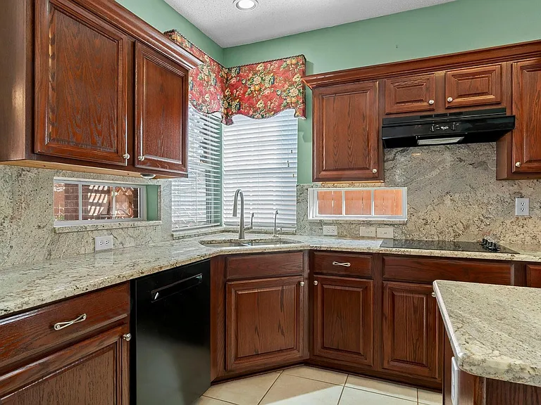 Kitchen featuring rich wood cabinetry, stone countertops, a stainless steel sink, a black cooktop, and a matching black range hood