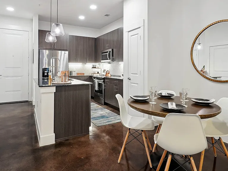 Apartment kitchen with stainless steel appliances and dining room with wood-style flooring.