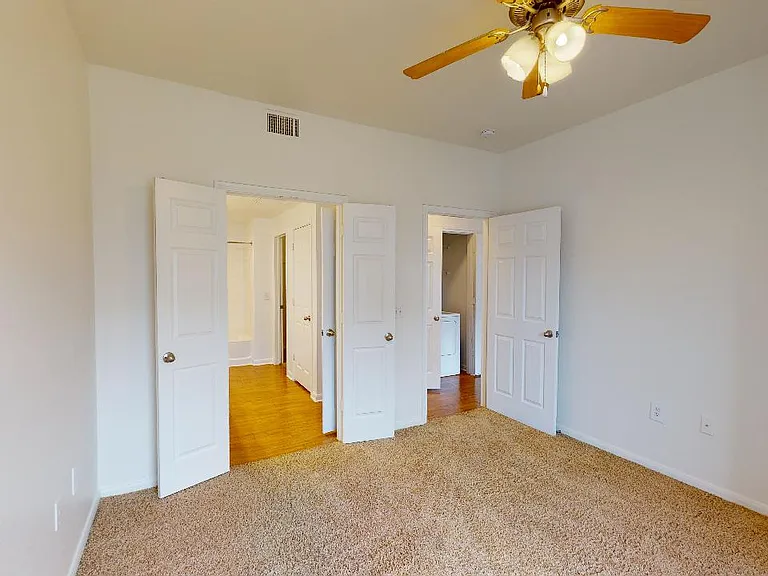 Spacious apartment bedroom with attached bathroom and plush carpet flooring.