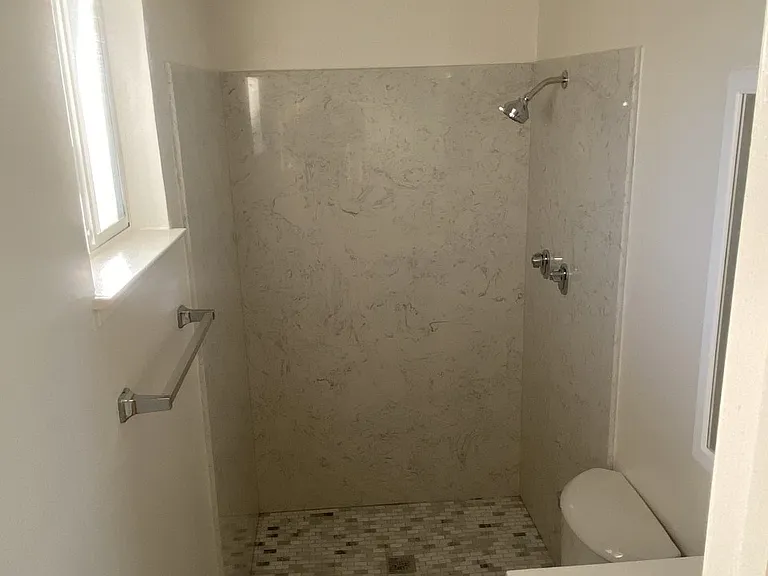 The master bath in this 2-bed, 2-bath suite offers tile flooring, a granite shower enclosure, updated mirrors, and a modern vanity with a sleek color palette. A window allows for natural airflow and added brightness.