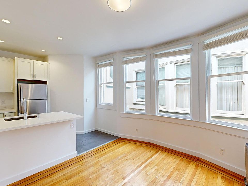 Living room with a large window, wood-like flooring, and a view of the kitchen