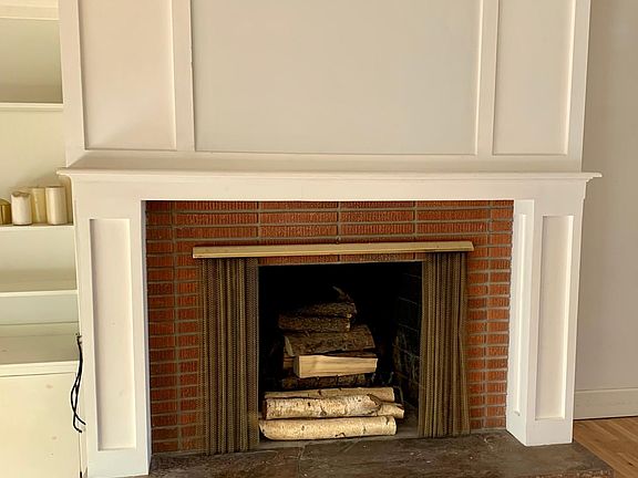 Living Room with wood burning fireplace and built in wood bookcase. Large custom floor to ceiling window to the left.