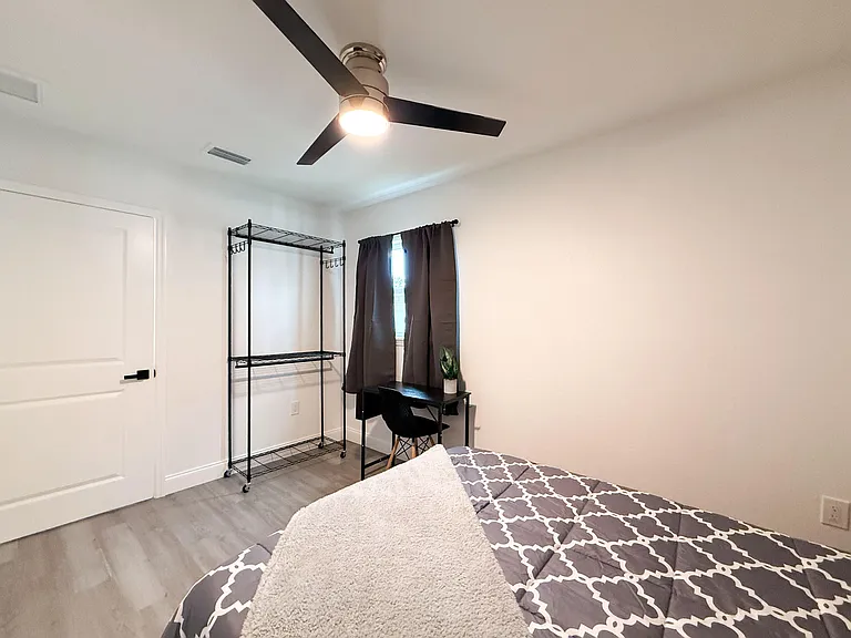 Bedroom includes a ceiling fan, window with curtains, a dedicated desk area, and open shelving for added storage.