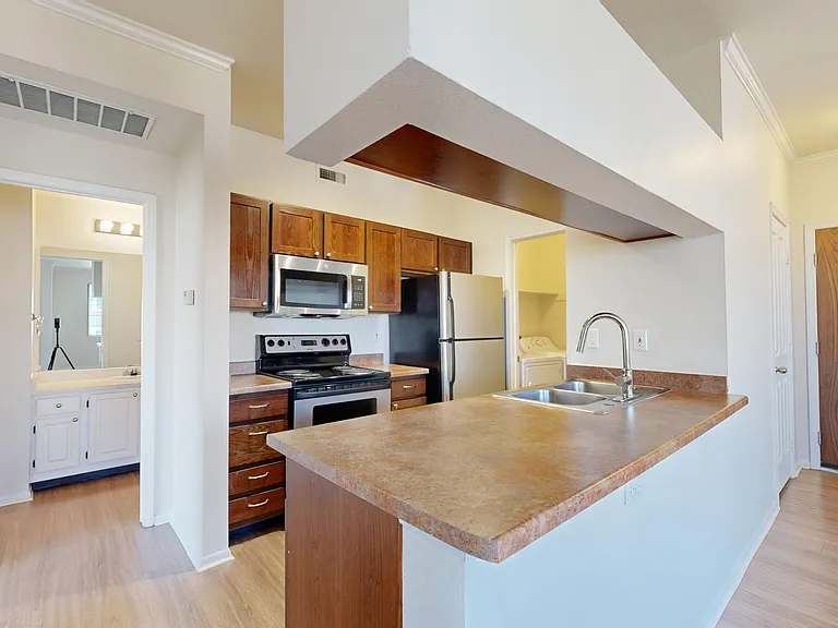 Apartment kitchen with stainless steel appliances and wood-style flooring.