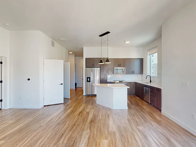 Apartment kitchen with stainless steel appliances, dining and living room with wood-style flooring.