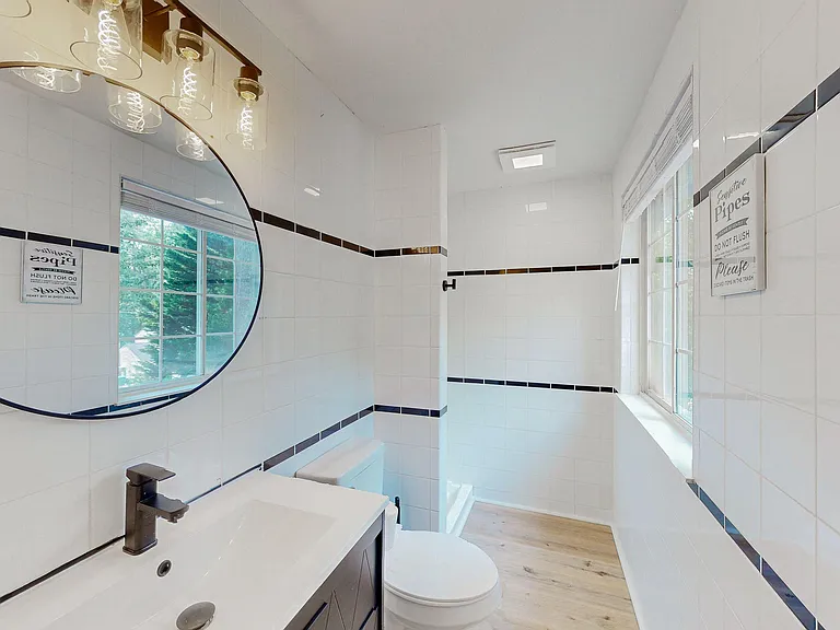 Tiled full bathroom with a tub/shower combo, updated vanity, and large windows that provide natural light and ventilation.