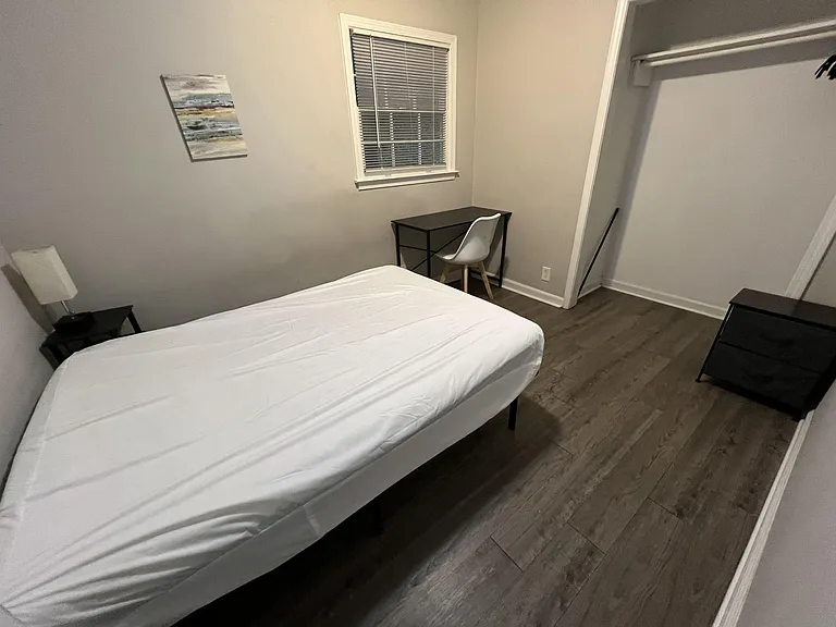 Furnished bedroom with a full-size bed, dedicated desk workspace, and an open closet for easy storage and organization.