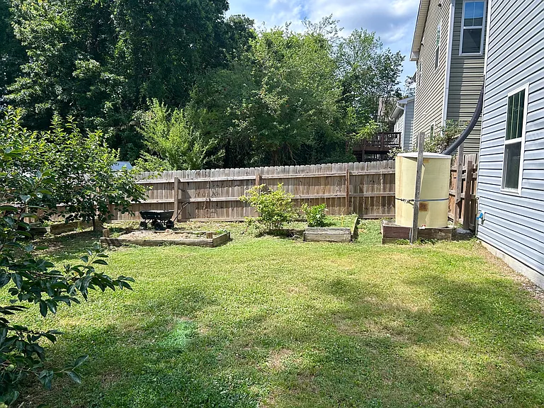 This is the first half of the garden space. Here you'll find raised planting beds, fig and persimmon trees you can eat from, and a 5_6 ft rain catcher for sustainable watering, perfect for anyone who loves to grow their own food!