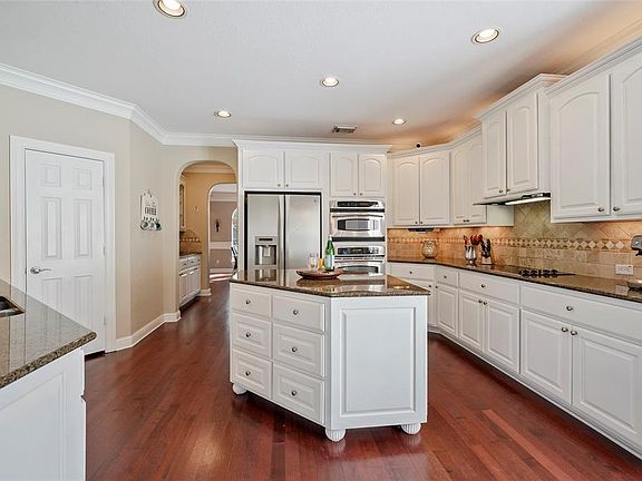 The Island Kitchen features an abundance of sleek, white cabinets accented with granite counters, designer backsplash and under mount lights.