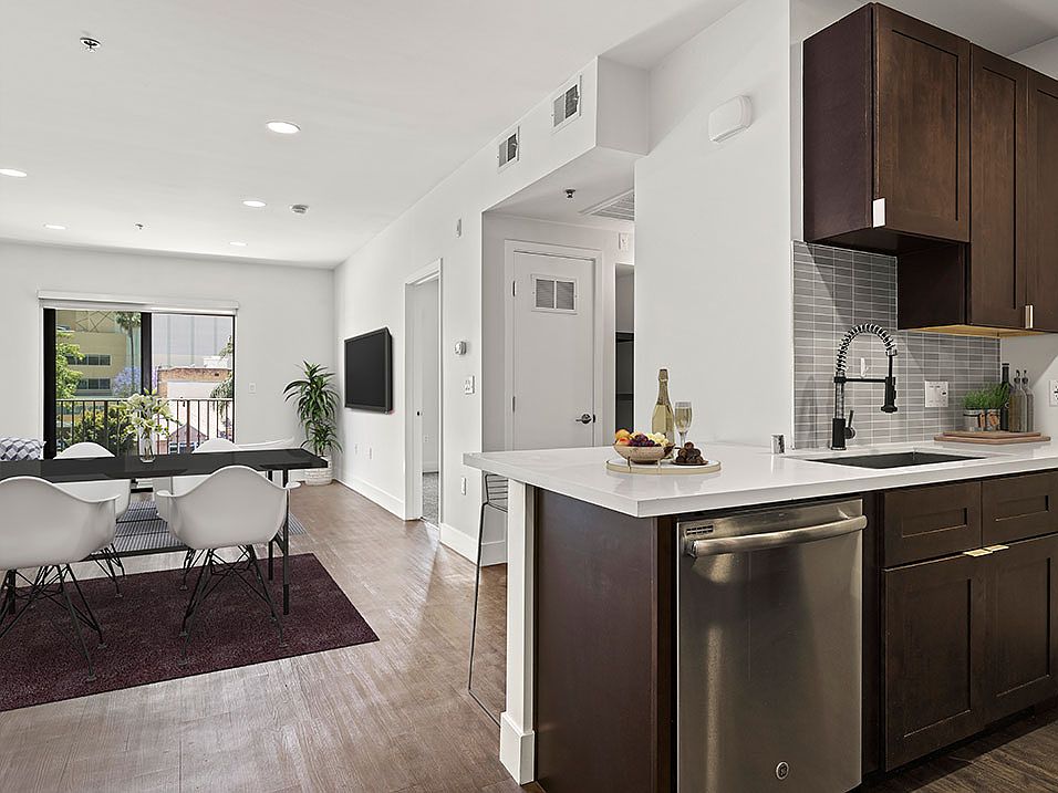 Tiled kitchen with stainless steel appliances and view of hardwood floored living room and balcony.