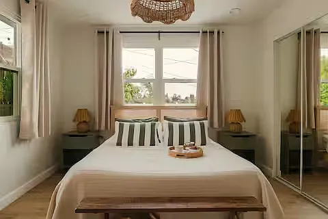 Inviting bedroom with a queen-sized bed and soft linens. Sunlight fills the room, and bedside lamps add warmth and a stylish, relaxed vibe.