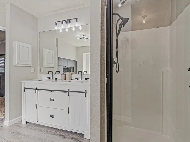 Bathroom featuring a white double vanity with barn-door style cabinet fronts, matte black fixtures, a large mirror, and a frameless glass shower enclosure