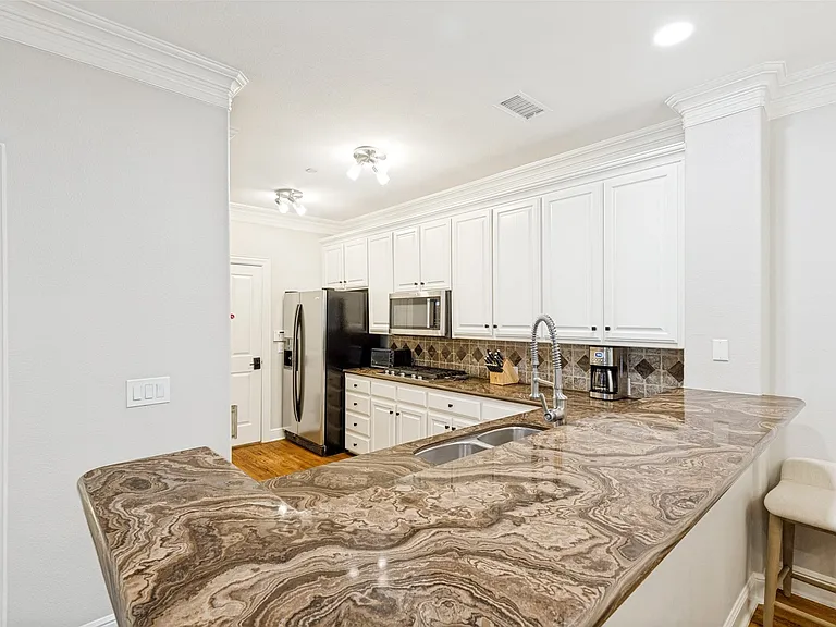 Kitchen featuring a double basin sink, expansive stone countertops, stainless steel appliances, white cabinetry with dark hardware, and a tiled backsplash