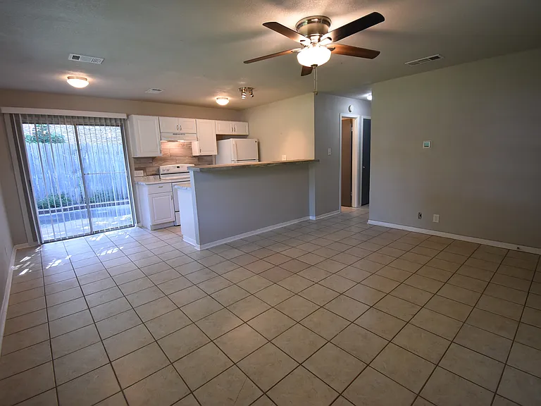 Open Floor plan! Living room with large windows and a ceiling fan. Kitchen in the background and Dining room with a sliding glass door that opens up to a cute patio.