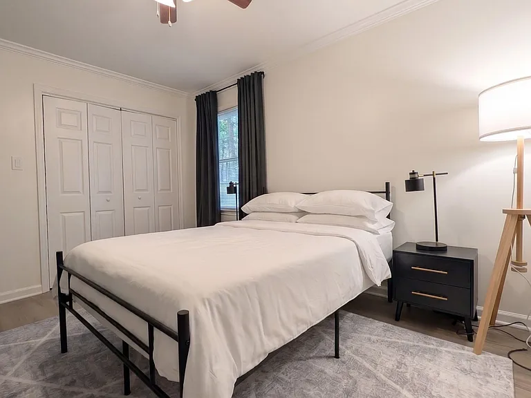 Well-appointed bedroom with a queen bed, nightstand lighting, ceiling fan, and double-door closet plus a window with drapes.