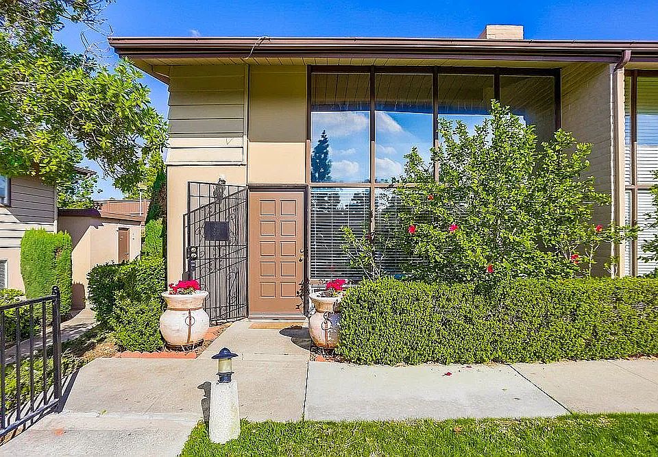 Beautifully landscaped entry with vibrant hibiscus and peaceful garden views. Vaulted ceilings and dramatic floor-to-ceiling windows flood the living room with natural light.