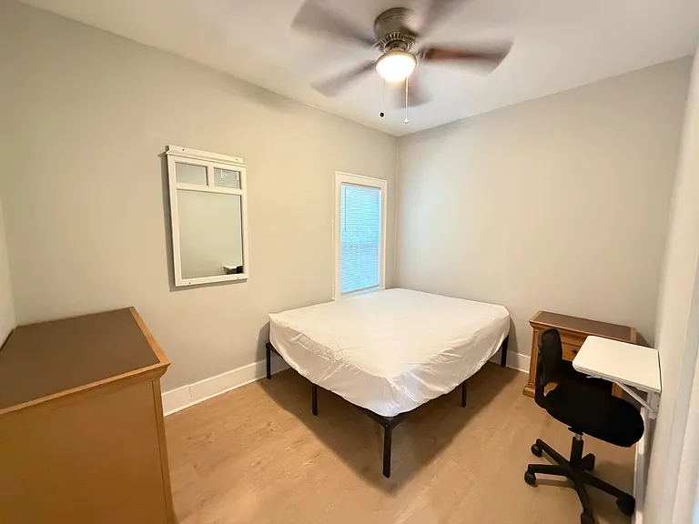 Furnished bedroom with a full bed, ceiling fan, and a window with blinds, plus a desk and dresser for easy storage.