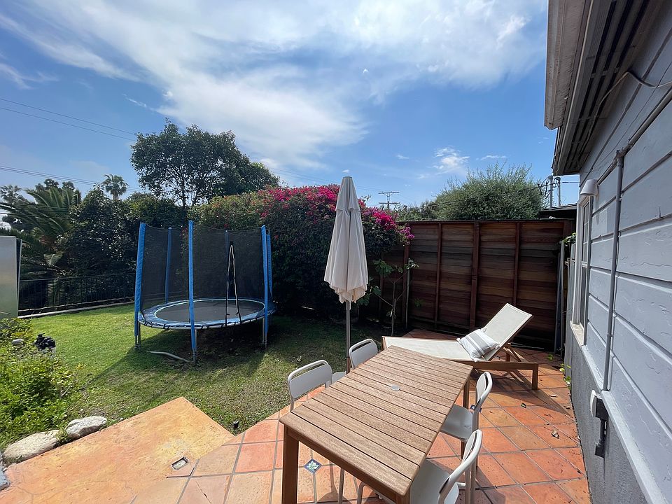 The backyard has a trampoline, a dining area, and a lounge chair.
