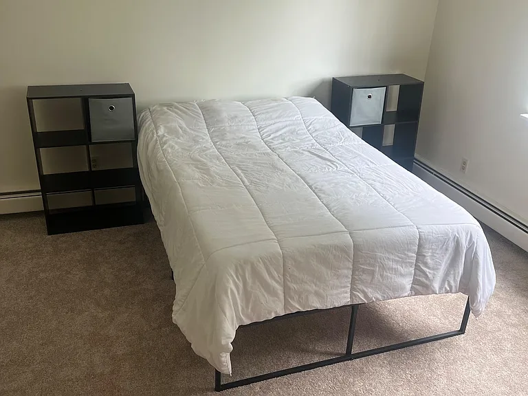 Furnished bedroom with a queen sized bed, bedside storage cubes, and wall space for a desk or dresser.