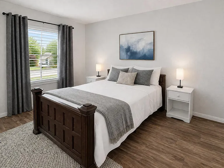 Furnished bedroom with a queen bed, matching nightstands, and a large window with blackout-style curtains.