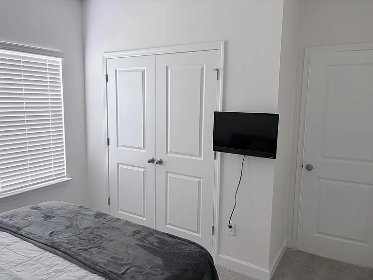 Bedroom with a double-door closet, wall-mounted TV, and a window with blinds for controlled natural light.