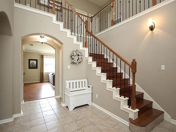 Open entry way with tile floors, wood staircase and neutral paint throughout home.