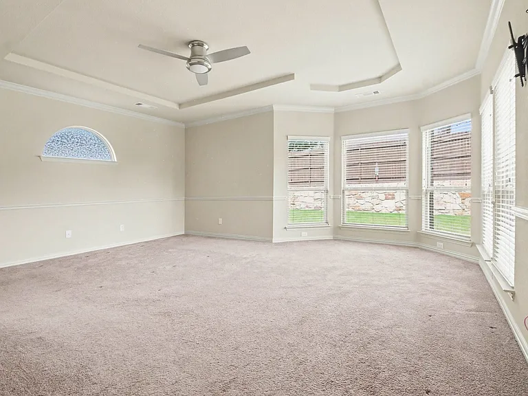 Spacious room featuring a tray ceiling with a ceiling fan, multiple windows with blinds, a decorative arched window, and neutral carpeting